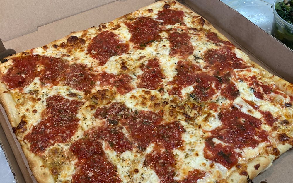 Square pie with dollops of tomato sauce over melted mozzarella, fresh out of the box